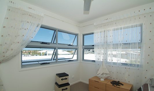 Grey framed awning windows in a room with sheer curtains